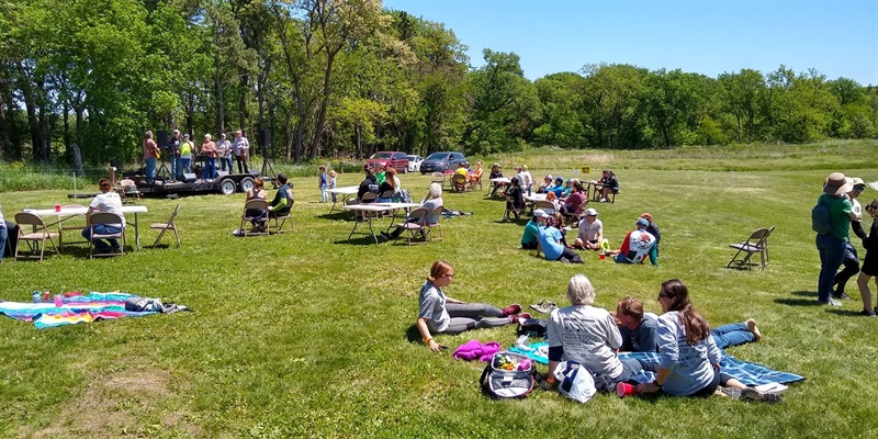 Groups of people sitting on grassy hill listening to a small band.