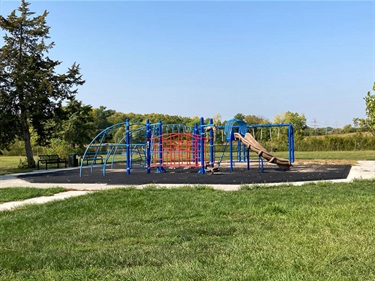Bowling Lake’s playground is located on the island in the middle of the park. The playground is on a rubber tiled surface and has a variety of climbing features and a slide. There are benches beneath large established evergreens.