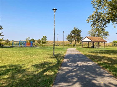 The island at Bowling Lake is accessible by a paved walking path. Also connected to the path are the park’s large playground and open shelter. Trees of various sizes provide shade, and light posts are dotted along the path.