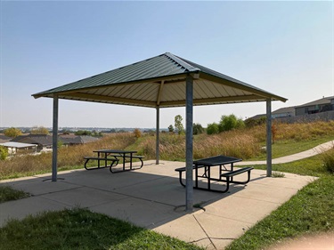 Ashley Park's open shelter is connected to a paved walking path and features a paved surface and picnic tables.