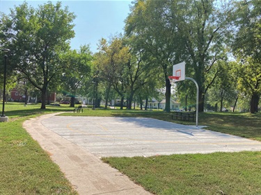 Half-Court Basketball hoop near a paved walking path and established shade trees.