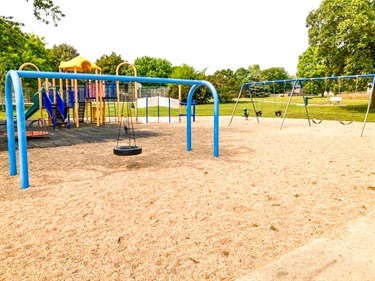 Filbert’s play area features a tire swing, belt and bucket swings on a sand play surface, adjacent, on a rubber tile surface is a multi level play structure with different slides and various climbing features.