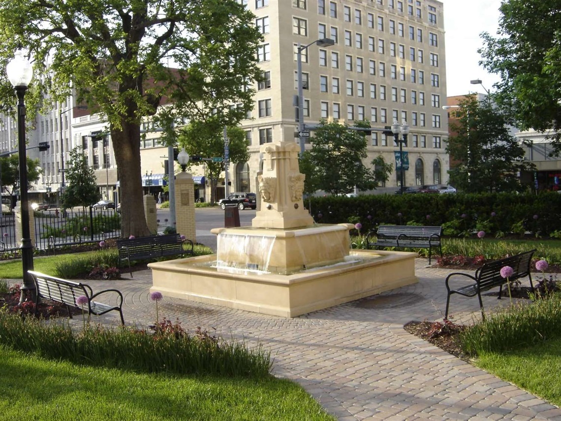 In the center of Government Square, there is a limestone fountain featuring Corn and Wheat Goddesses from the 1920's. Benches surround the fountain and alliums bloom behind them.