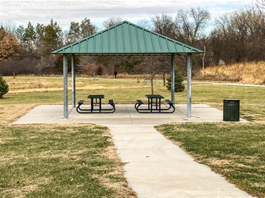 This open shelter has picnic tables and a concrete pad connected to a paved path.