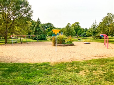This circular play area features funnel ball, swings, multi level playground structure, and swings. The center of the circle features a flowerbed.