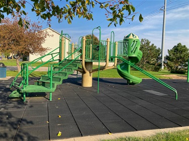 A multi level platform playground includes spiral slide and several climbing features. Rubber tiles have been laid in the play area.