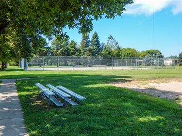 Bleacher seats are located near the paved walking path and ball field.