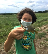 A young Nature Center camper shows the small fish they caught. The fish is about the same size as the campers hand.