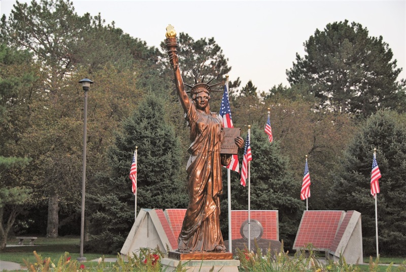 A bronze Lady Liberty statue stands tall in the middle of the garden. Behind her are American flags and more memorials.