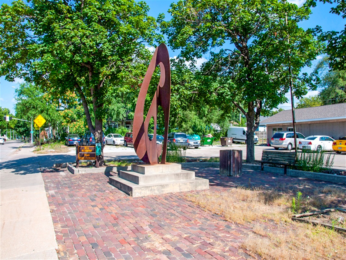 Dan Peragine's Noos stands in the brick paved plaza of Bea Richmond, this cor-ten steel structure is tall and features many curved and straight cut outs that change shapes as you move.