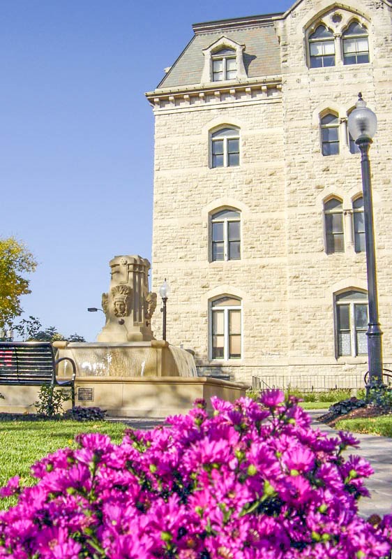 Vibrant purple asters bloom in-front of the square's fountain as the historic building fills in the background. 