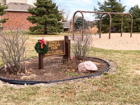 A brown park sign sitting in a flower bed of hardy perennials reads, “Stephen C. Schleich Park