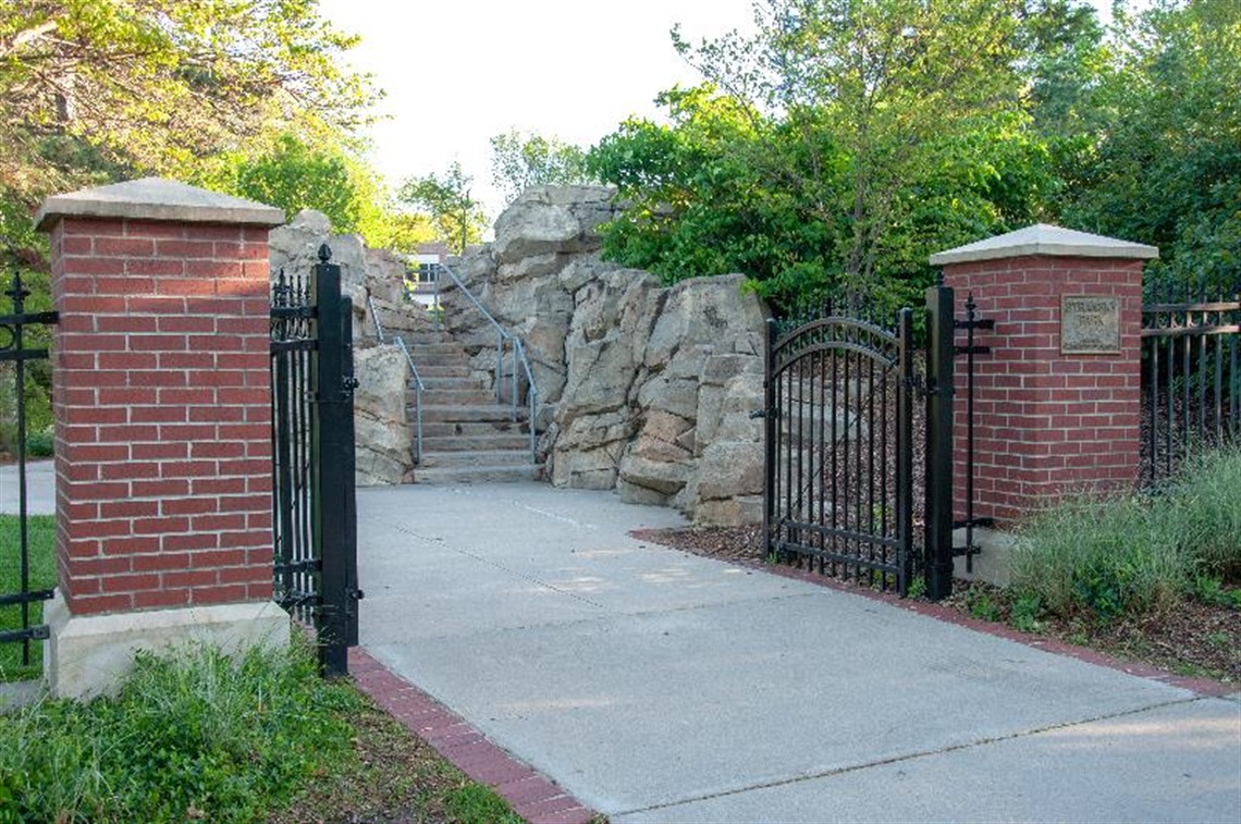Park gated entrance opens into a paved walkway with limestone boulder wall with stairs leading to the top.