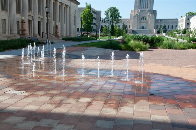 Streams of water shoot up from the bricks paving the ground with part of the Capitol building in the background