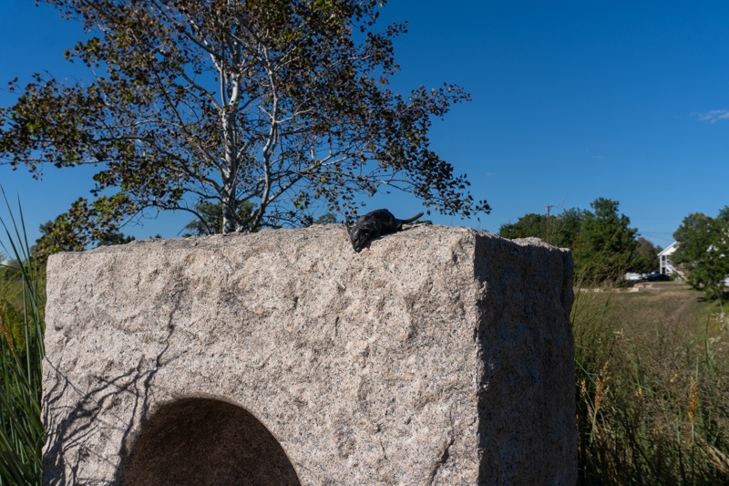 wide shot of a bronze mouse on top of a stone in a park