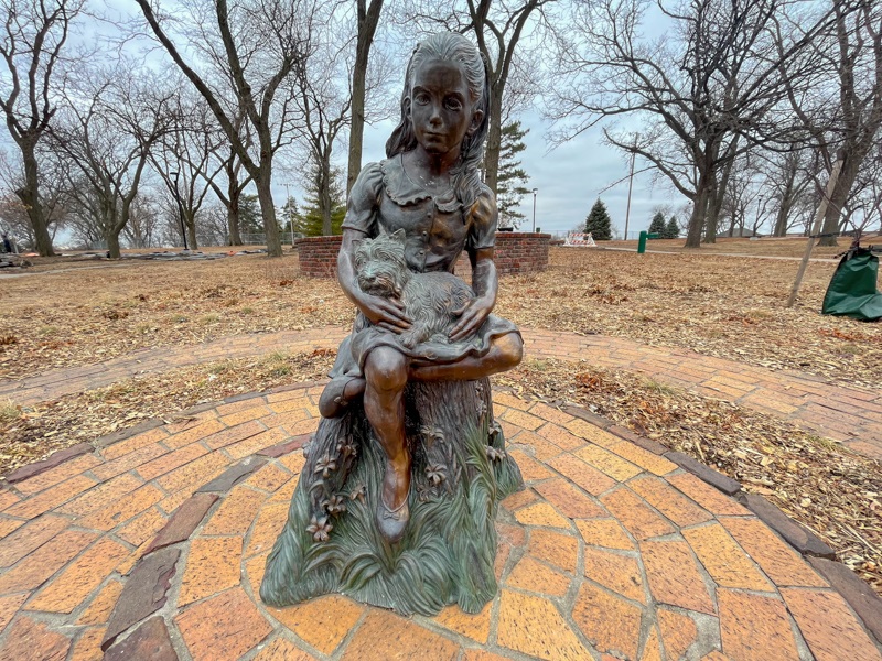 A statue of a young girl with a dog in her lap, sitting on a metal stump.