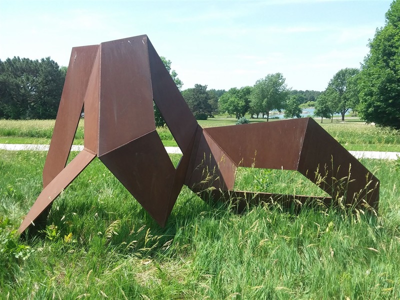 The brown, steel geometric sculpture in a patch of grass at Holmes Lake Park