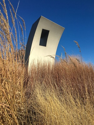 Looking through fall grasses, the metal form discover stands