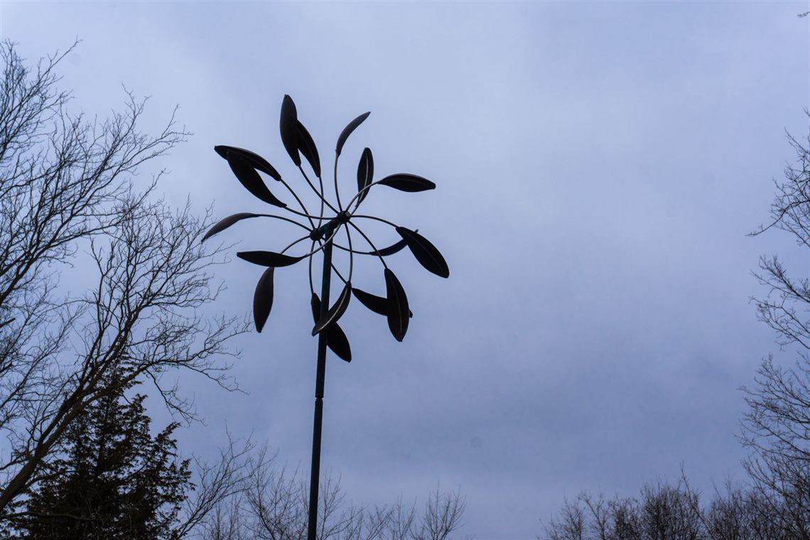 A double-sided wind sculpture made up of feather like pieces that spin, creating an almost flower like shape. 