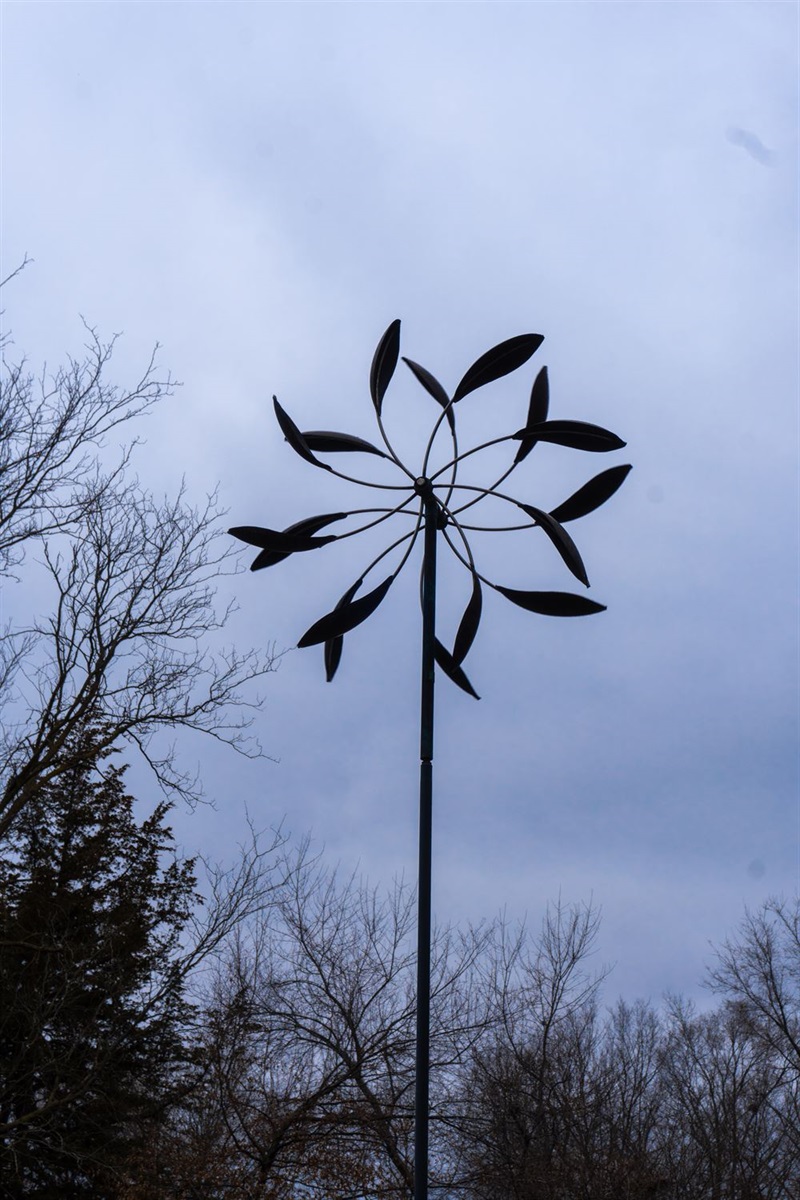 A double-sided wind sculpture made up of feather like pieces that spin, creating an almost flower like shape. 