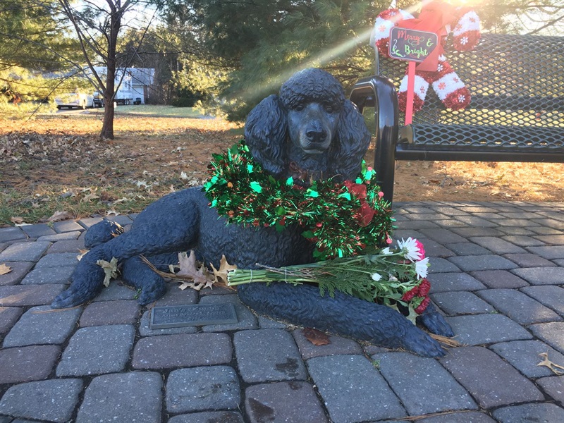 A bronze dog laying on the ground with flowers and a wreath decorating it. 