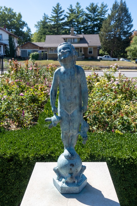 A young child, smiling in the sunlight, holding two frogs while standing on a pedestal