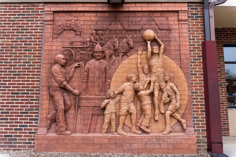 The mural of kids playing basketball and historical firefighters made out of brick