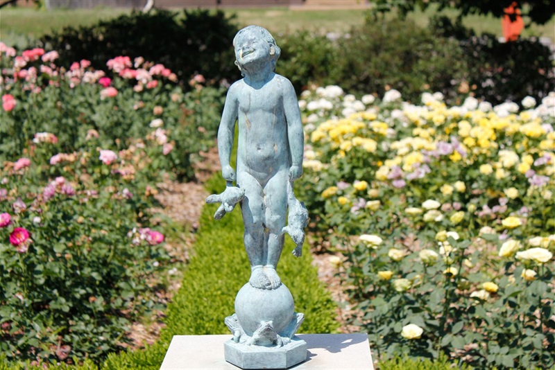 The sculpture Frog Baby surrounded by roses in the Rose Garden