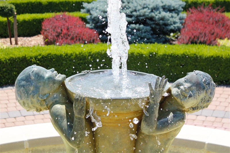 A close up of the fountain and the faces on the Joy Fountain by Edith Parsons. It shows two children displaying pure joy while playing in the water while holding the fountain up.