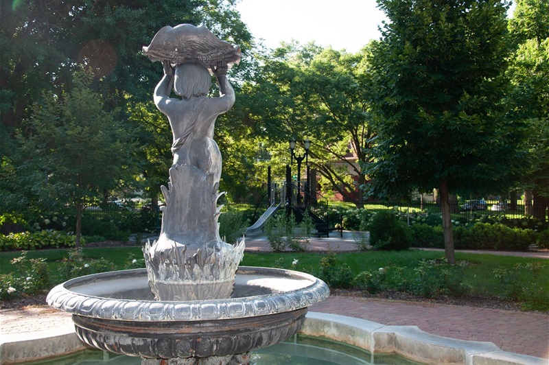 The backside of the cherub fountain, the cherub is lifting a shell over it's head and the base has water flora details. 