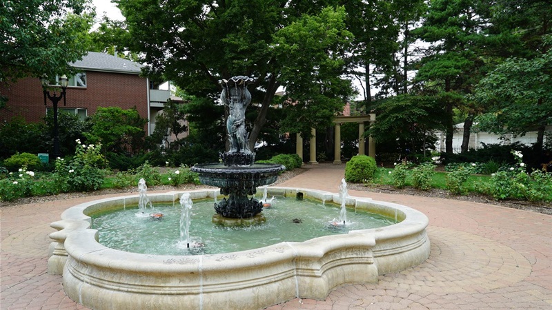A fountain featuring a cherub holding a shell over its head while standing on a pedestal in the middle of the large pool of water. 