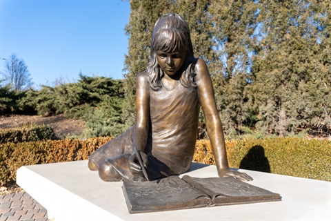 A young girl captured in bronze, drawing in a sketchbook, while lounging. 