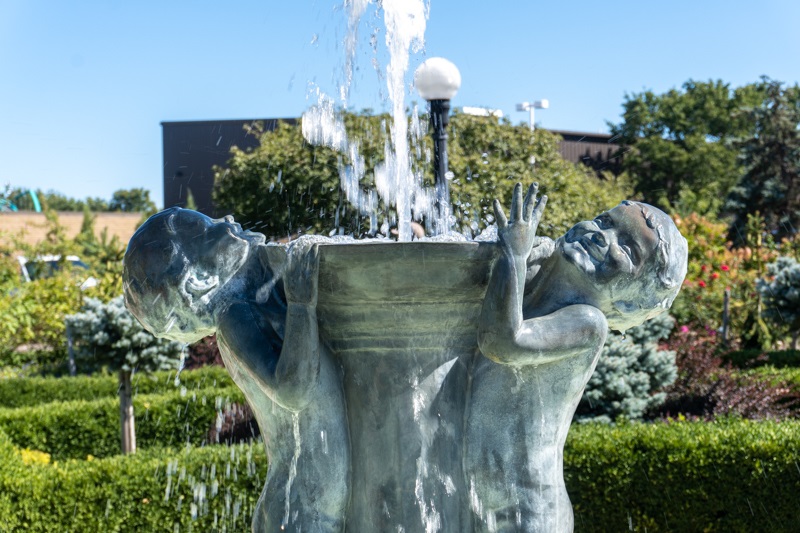 A close up of the fountain and the faces on the Joy Fountain by Edith Parsons. It shows two children displaying pure joy while playing in the water while holding the fountain up.