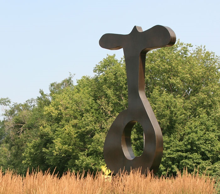 a large bronze sculpture that is vaguely key-shaped, surrounded by grass with trees in the background.