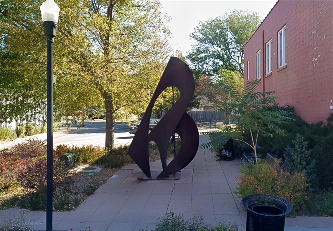 Amidst various greenery rises a steel abstract sculpture