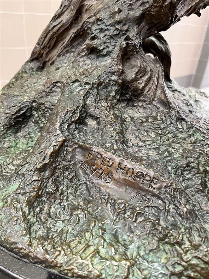 A close up of the base of a sculpture which appears to be a rocky texture with a block of wood extending from the top. There is a signature engraved in it that says Fred Hoppe, 1998, 17/50