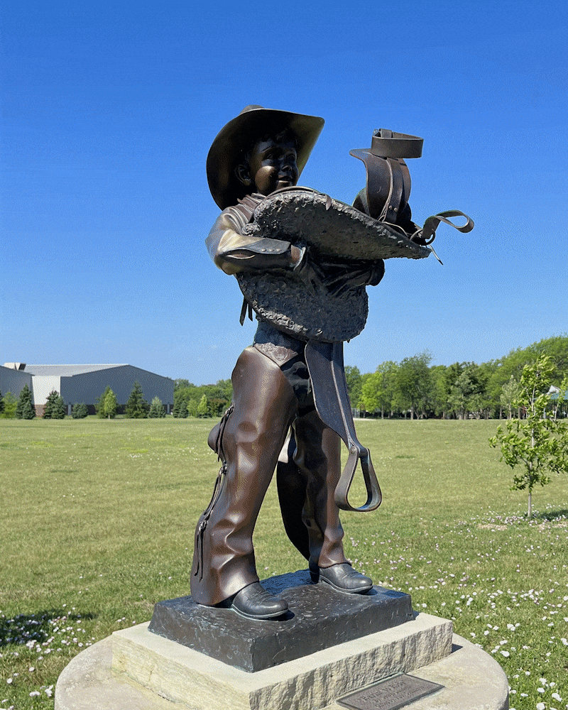 Rotating around a sculpture of a young cowboy holding a saddle in his arms. 