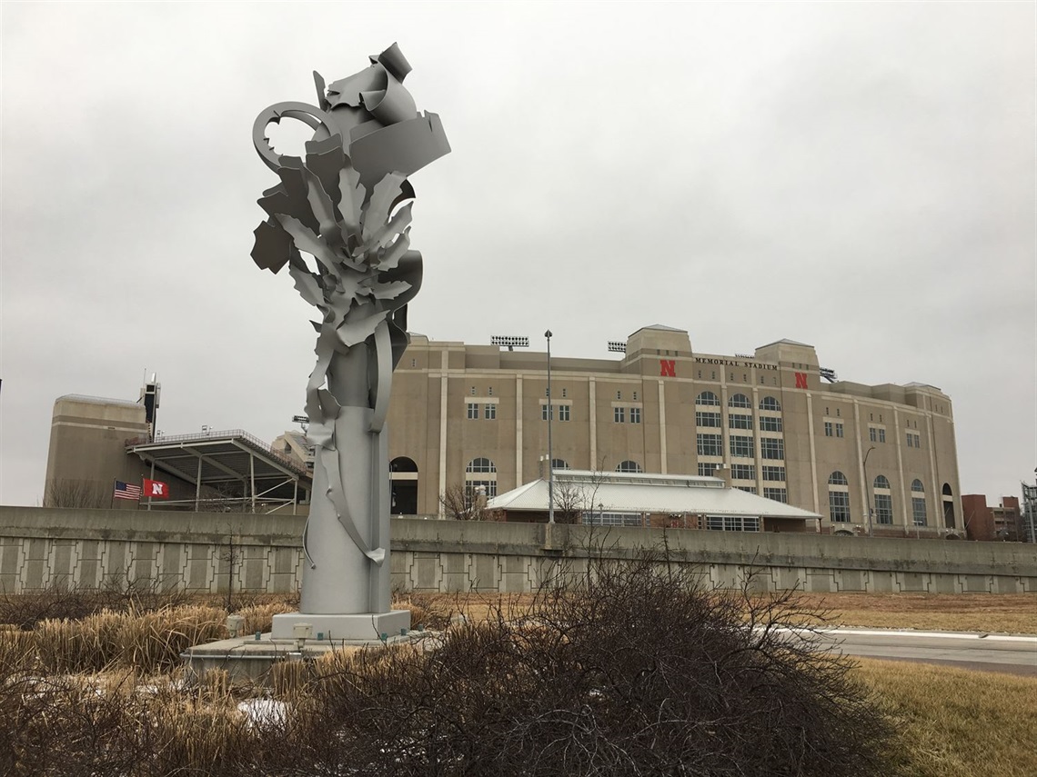 An tall abstract metal sculpture with Memorial Stadium in the background.