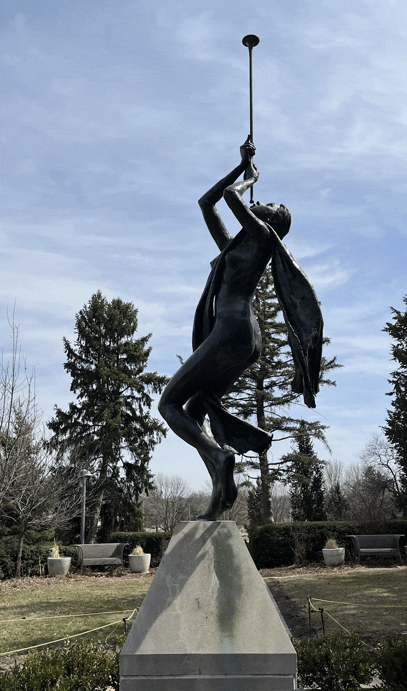 Rotating around a sculpture of a young nude woman with a draped fabric blowing into a horn straight into the air. 