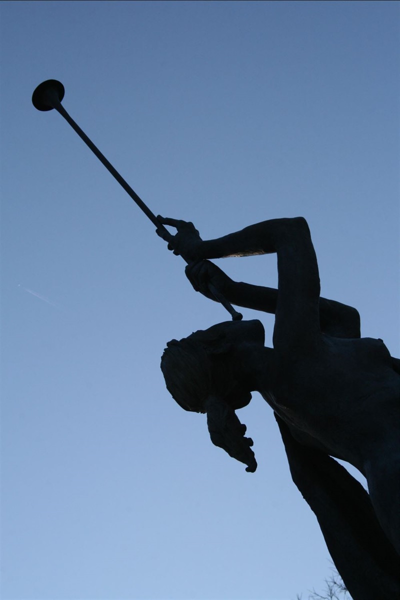 sculpture of a woman blowing into a bugle which is lifted above her head