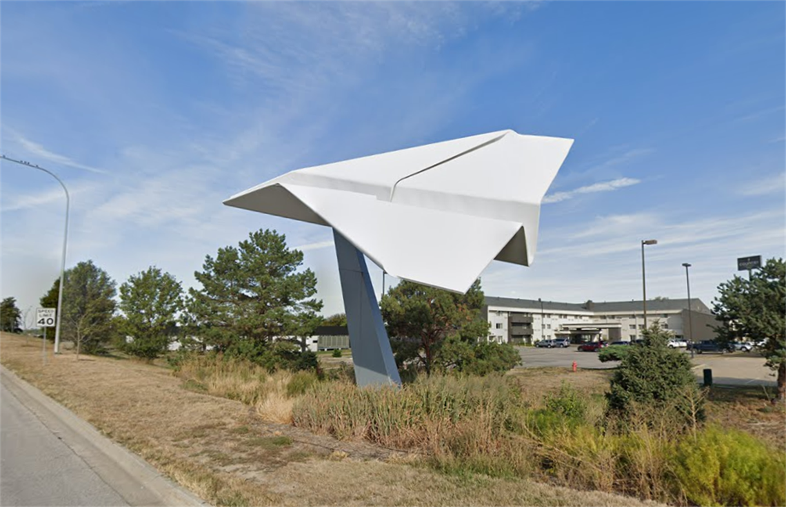 A giant paper airplane made of metal on the side of a road