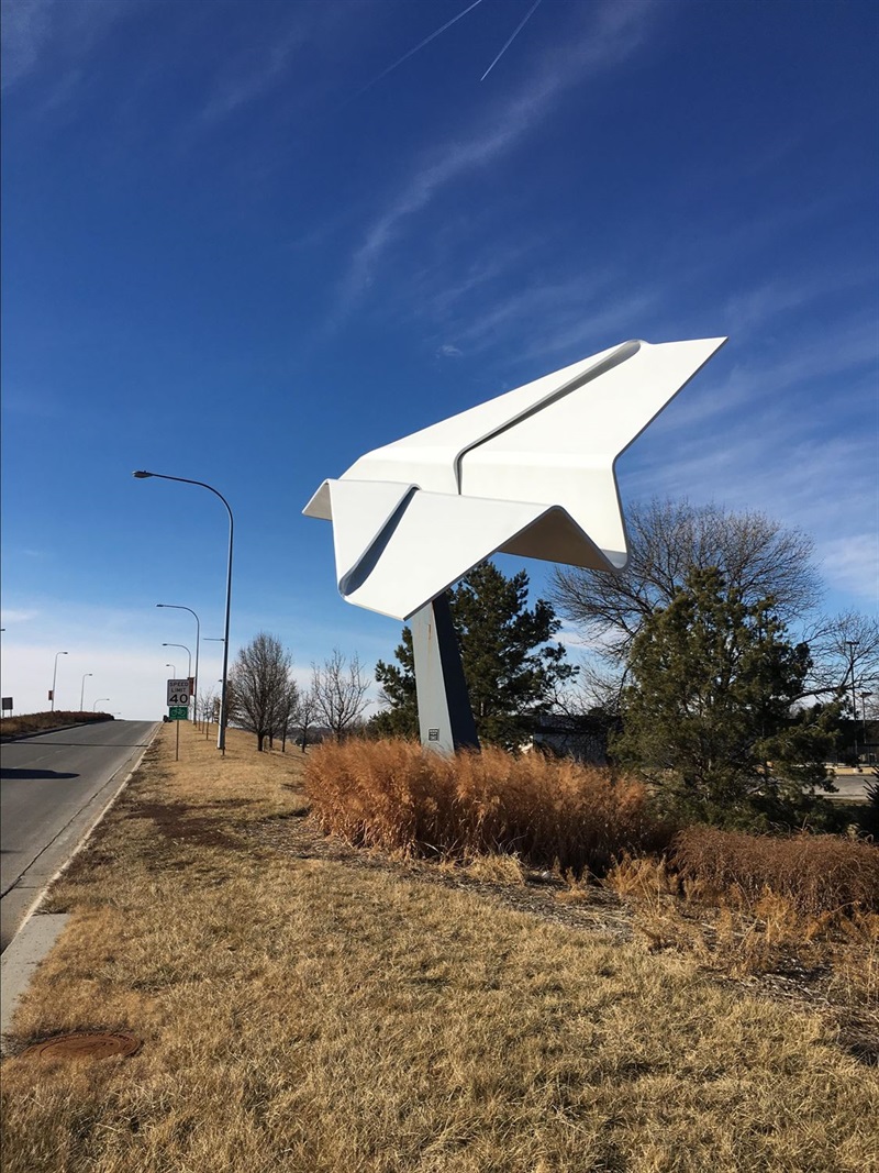 A giant paper airplane made of metal on the side of a road