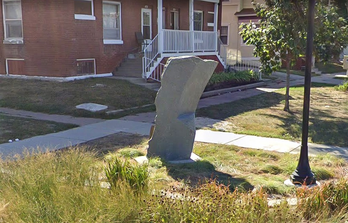 A slab of sculpted granite rises from the grass from a slight distance.