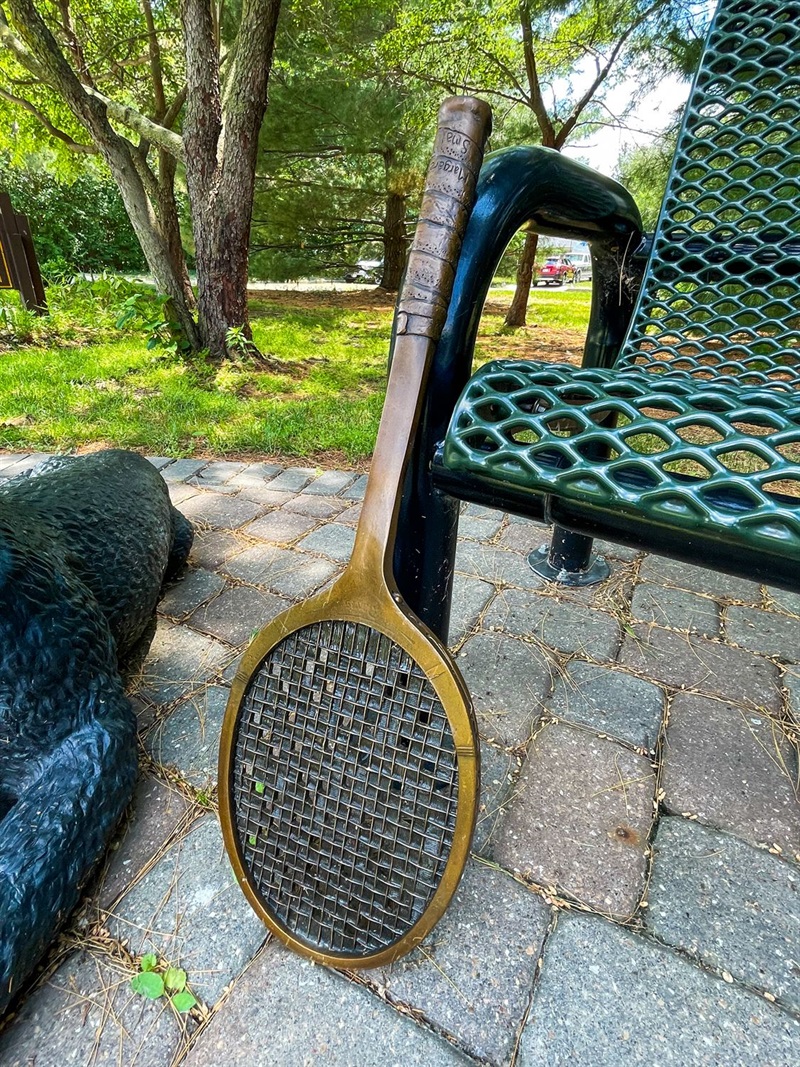 A bronze tennis racket leaning up against a park bench.