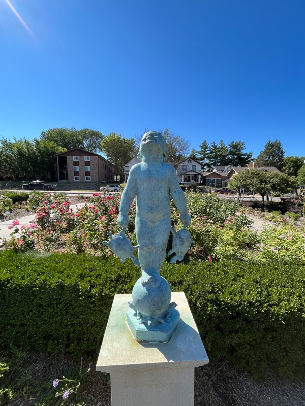 A sculpture of a young child smiling in the sunlight, holding a turtle in each hand