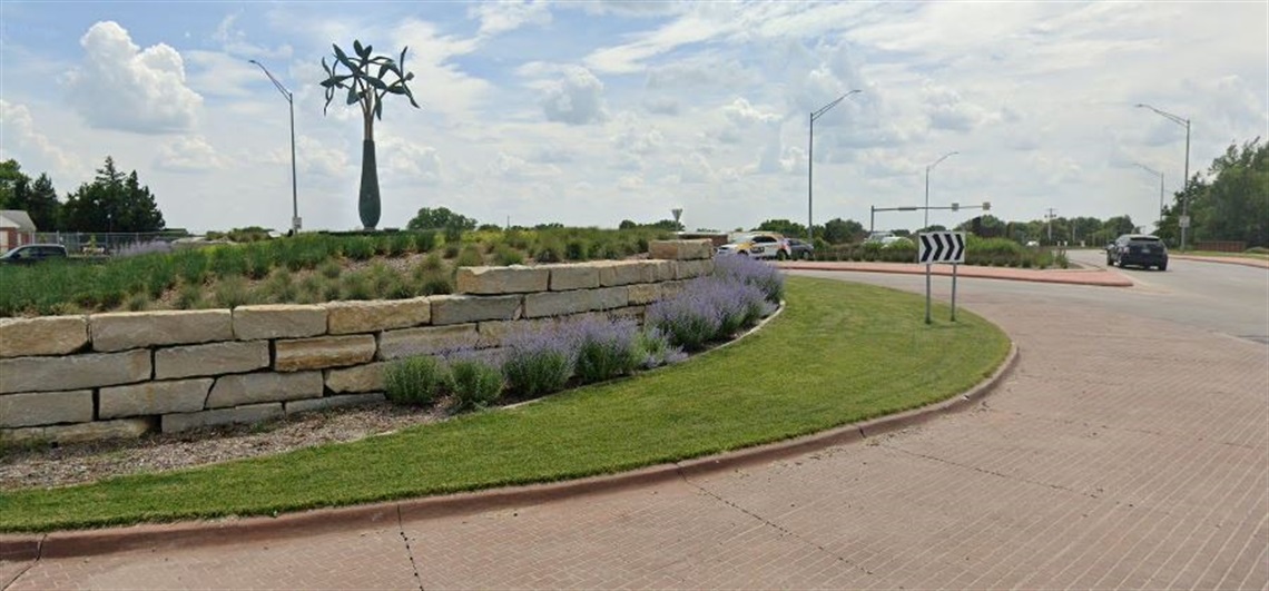 in the middle of a roundabout, rises a larger than life sculpture of a vase with flowers in it.