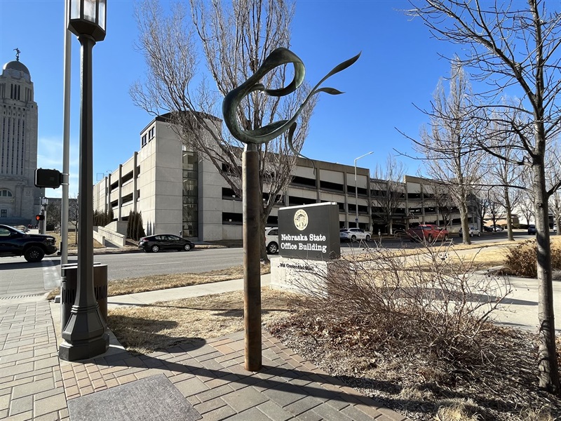 A twisting sculpture atop a pole amidst trees and poles.