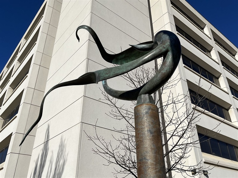 A twisting metal figure standing in front of a cream building.
