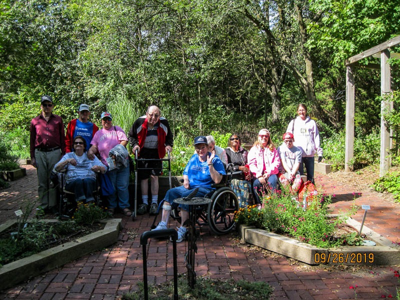 Day Structure enjoys their outing to the Nature Center's Herb Garden. The group poses for a picture among the beds.