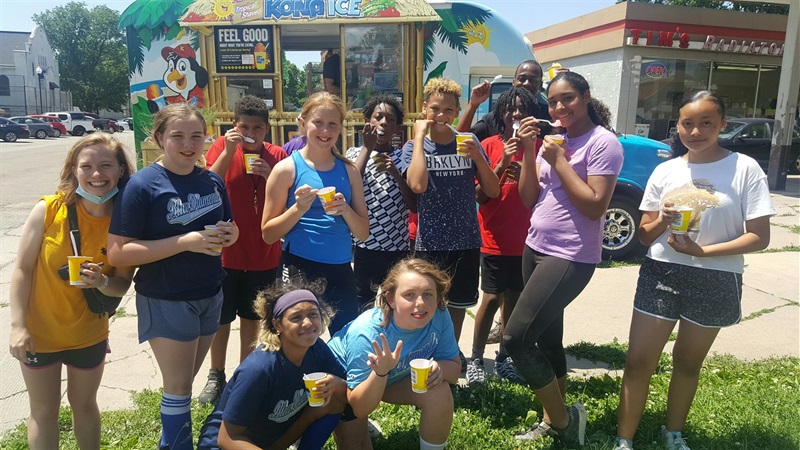 Campers pose in front of Kona Ice, enjoying a refreshing treat on a warm sunny day.